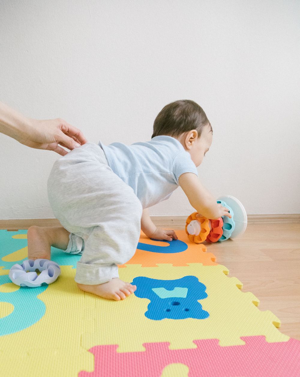 Een baby kruipt over een kleurrijke speelmat naar een speeltje
