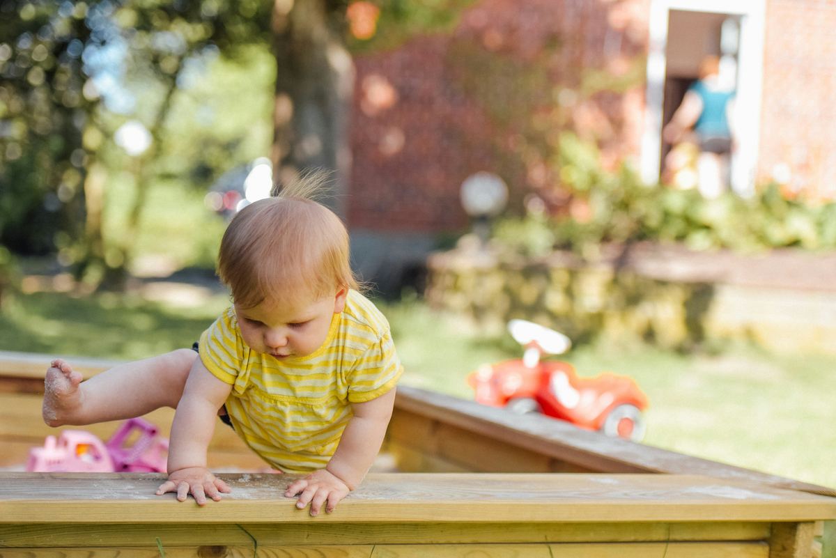 Een baby klimt over de rand van een zandbak in een tuin